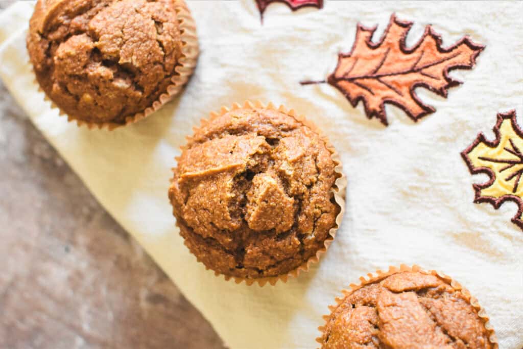 Three muffins on a fall-leaf print kitchen towel.