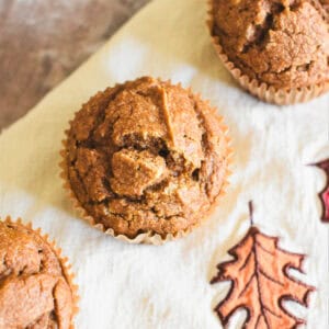 Pumpkin muffins on a kitchen towel decorated with fall leaves.