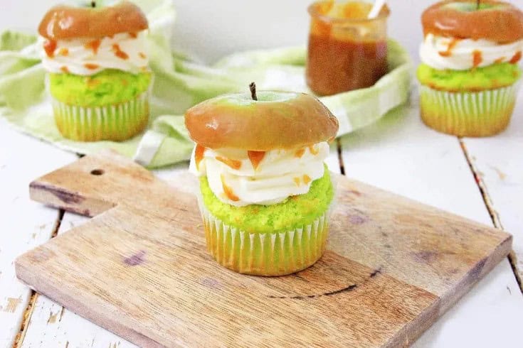 A caramel apple cupcake on a wooden board with more behind it.