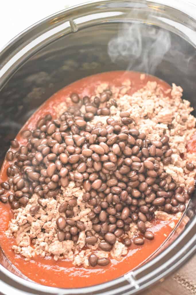 Canned tomatoes, ground pork, and black beans in a crockpot.