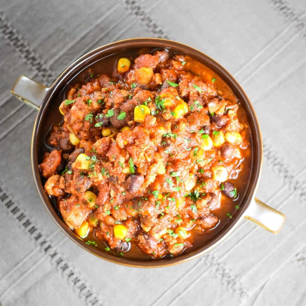 A serving of pork chili in a bowl on a dark kitchen napkin.