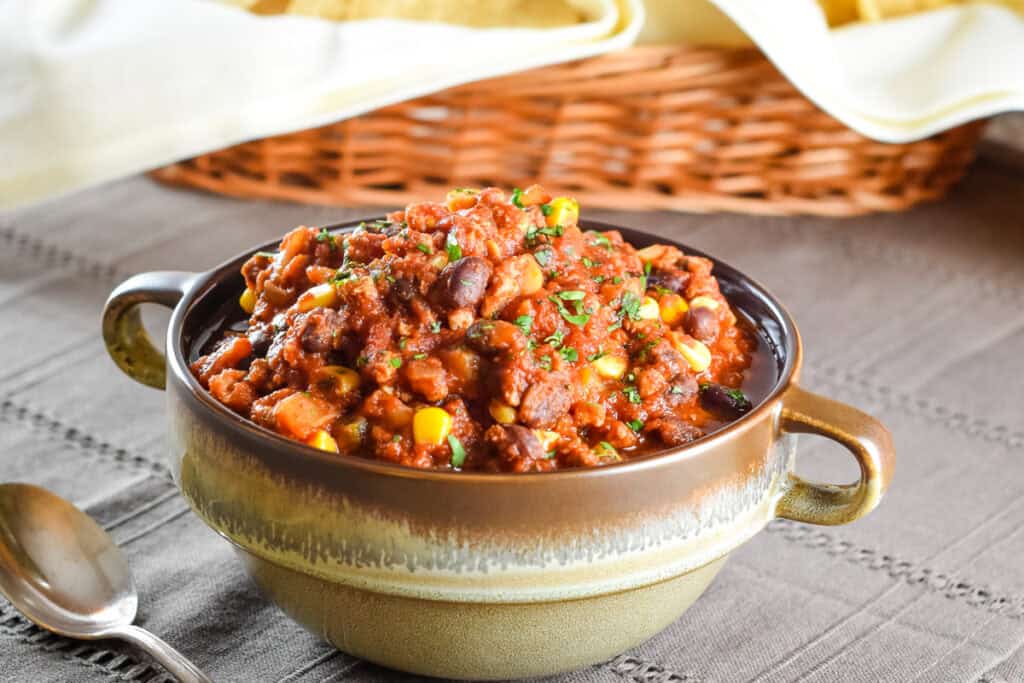 Ground pork and black bean chili in a bowl with a spoon next to it.