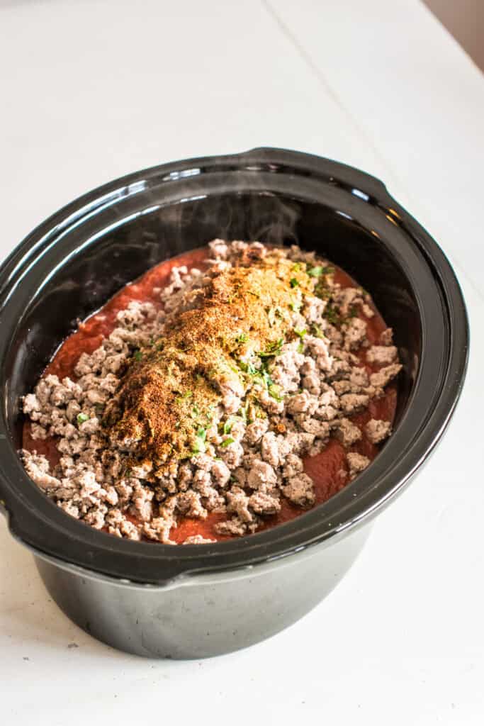 Crushed tomatoes, turkey, and seasonings added to veggies and beans in a slow cooker.