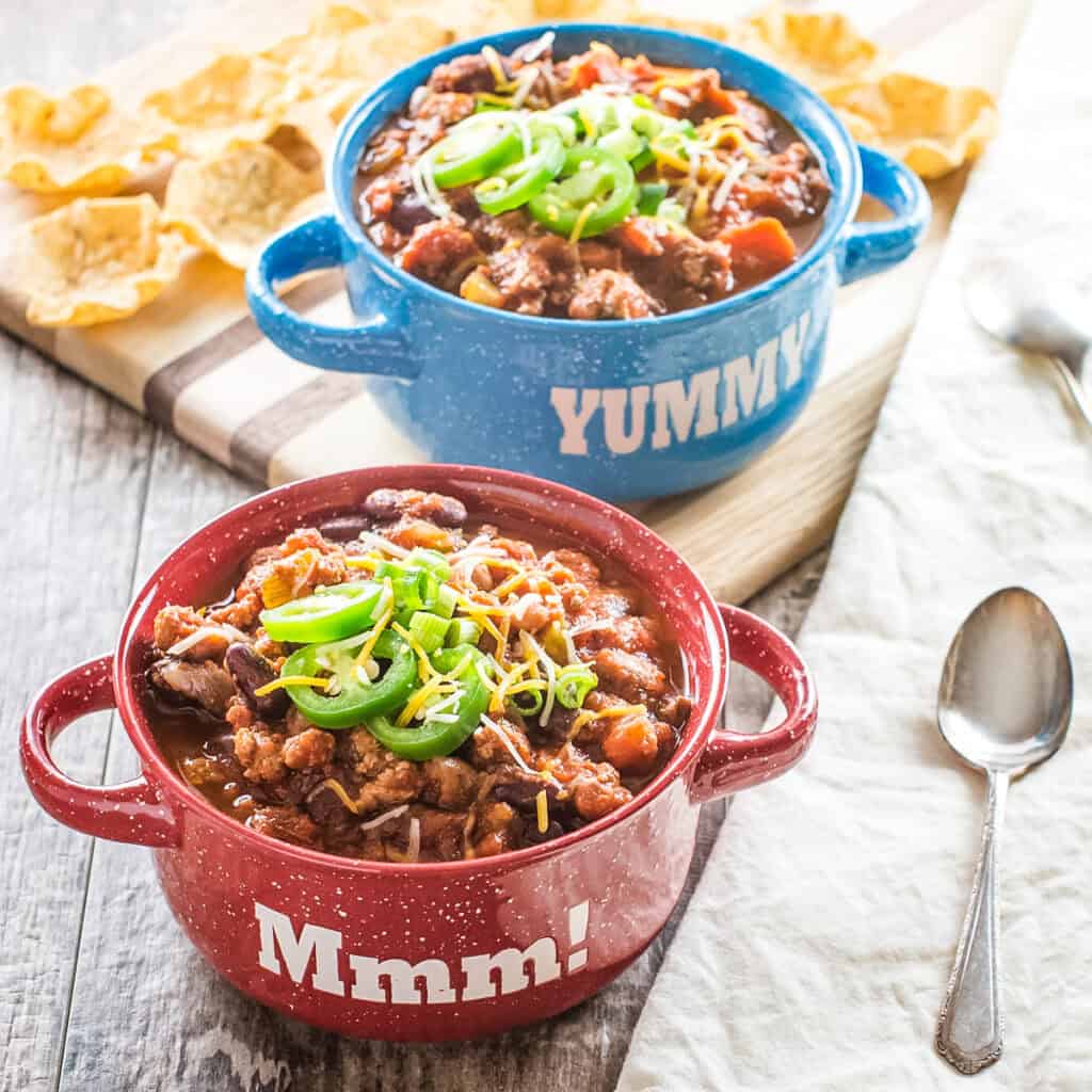 A red and blue bowl of turkey chili and tortilla chips in the background.