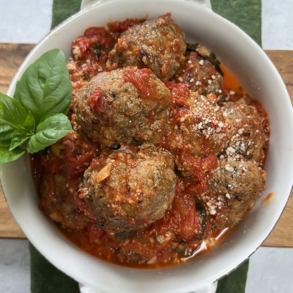 Pan fried meatballs with marinara sauce in a white bowl.