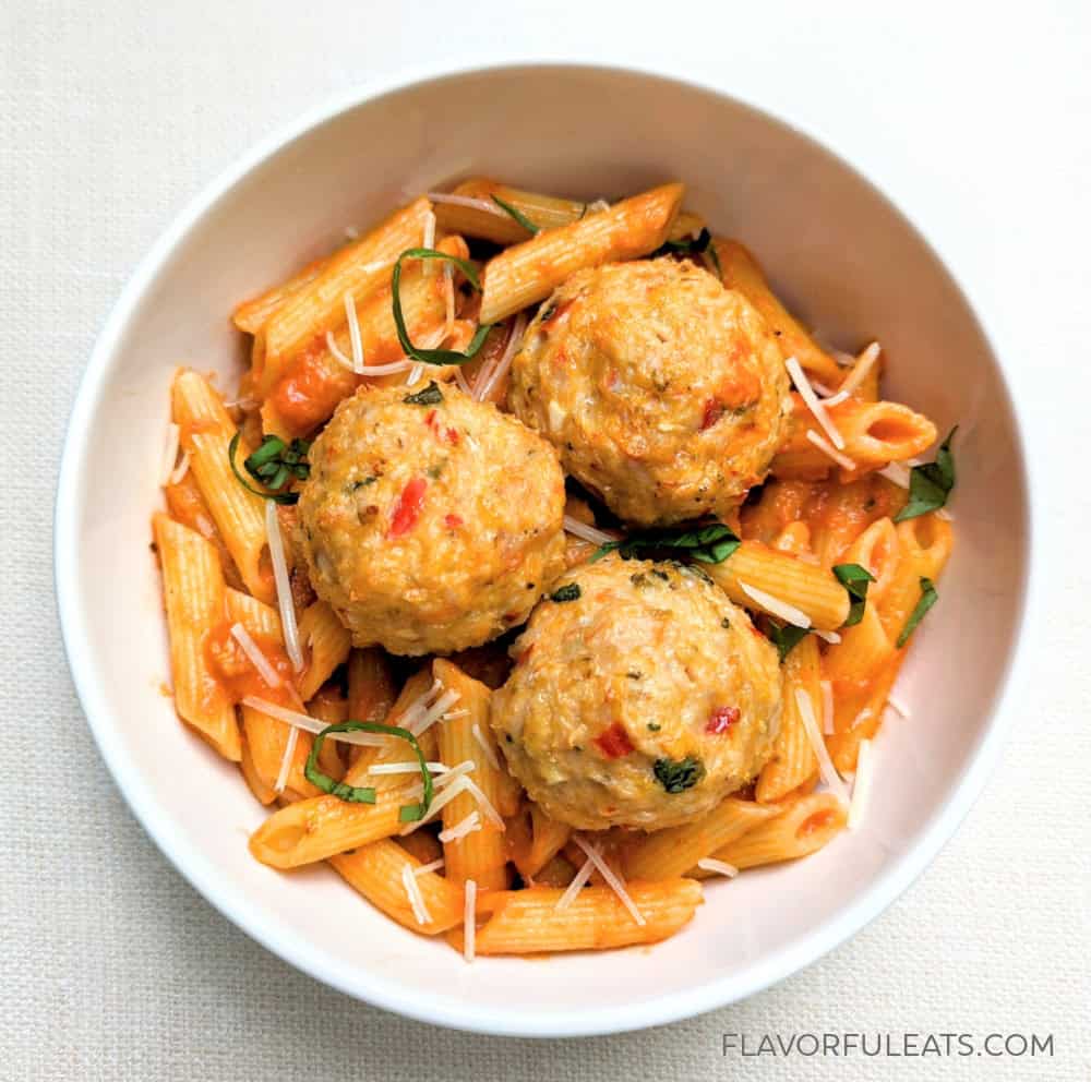 Calabrian meatballs on top of penne pasta in a white bowl.