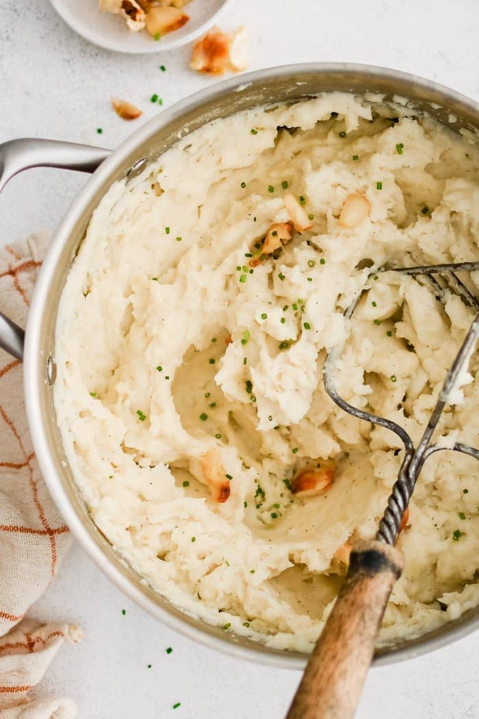 Roasted garlic mashed potatoes in a bowl with a potato masher.