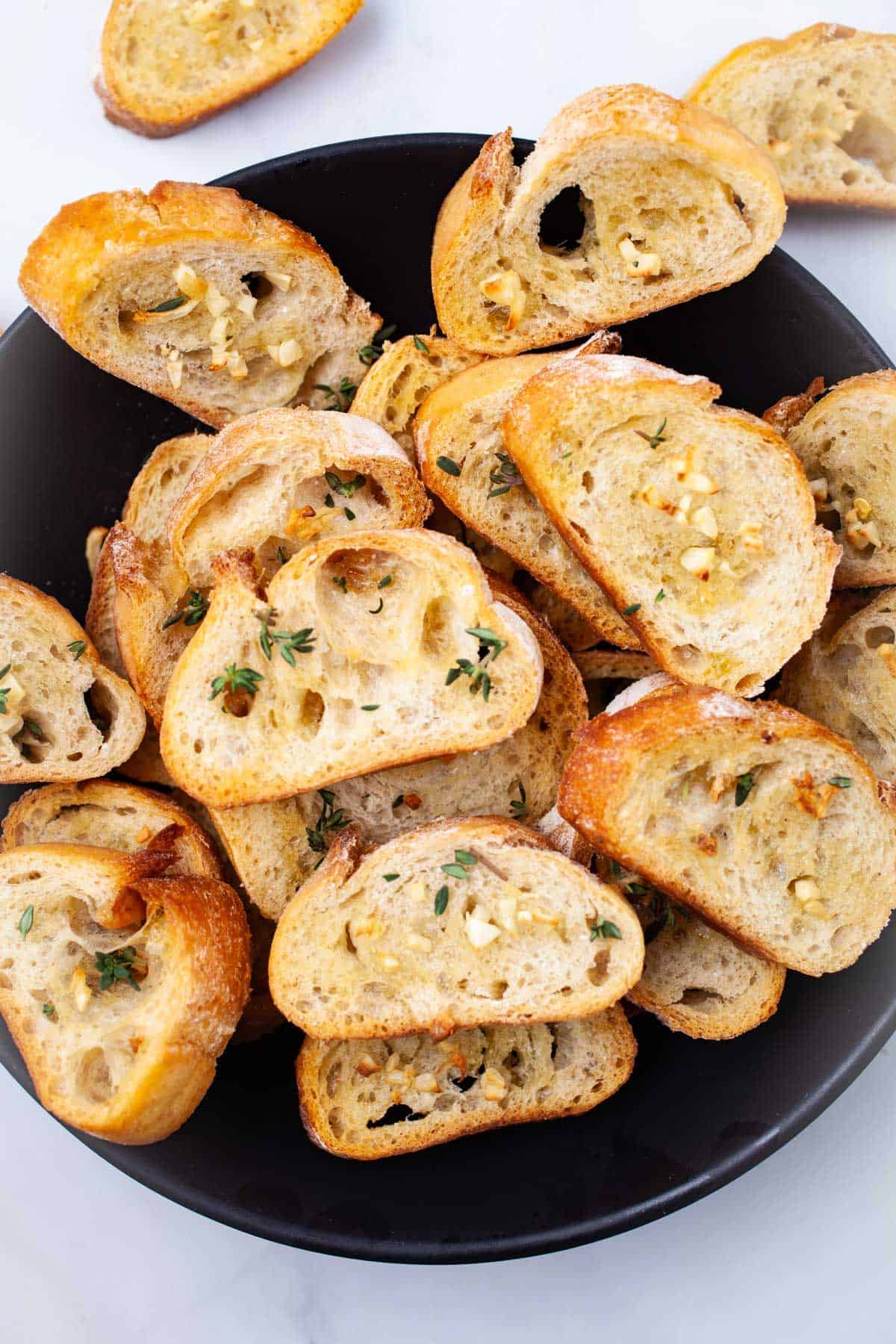 Pieces of garlic crostini on a black serving dish.