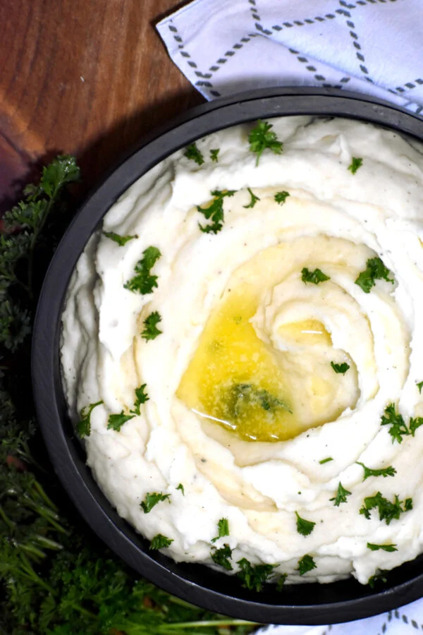 Goat cheese mashed potatoes in a black bowl with melted butter and parsley garnish.