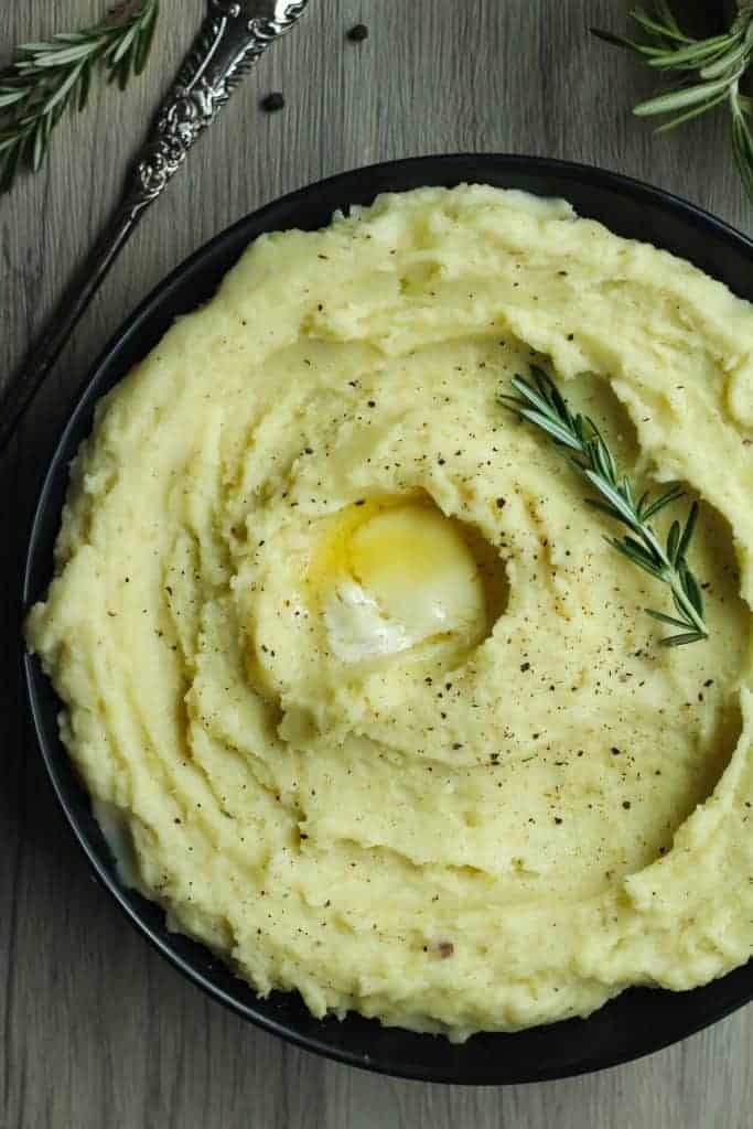 Rosemary garlic mashed potatoes in a black bowl with a rosemary sprig on top.