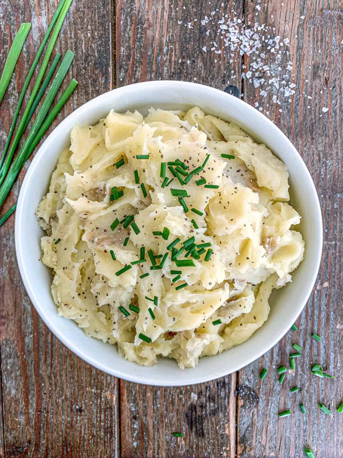 Truffle mashed potatoes in a white bowl with chives on top.