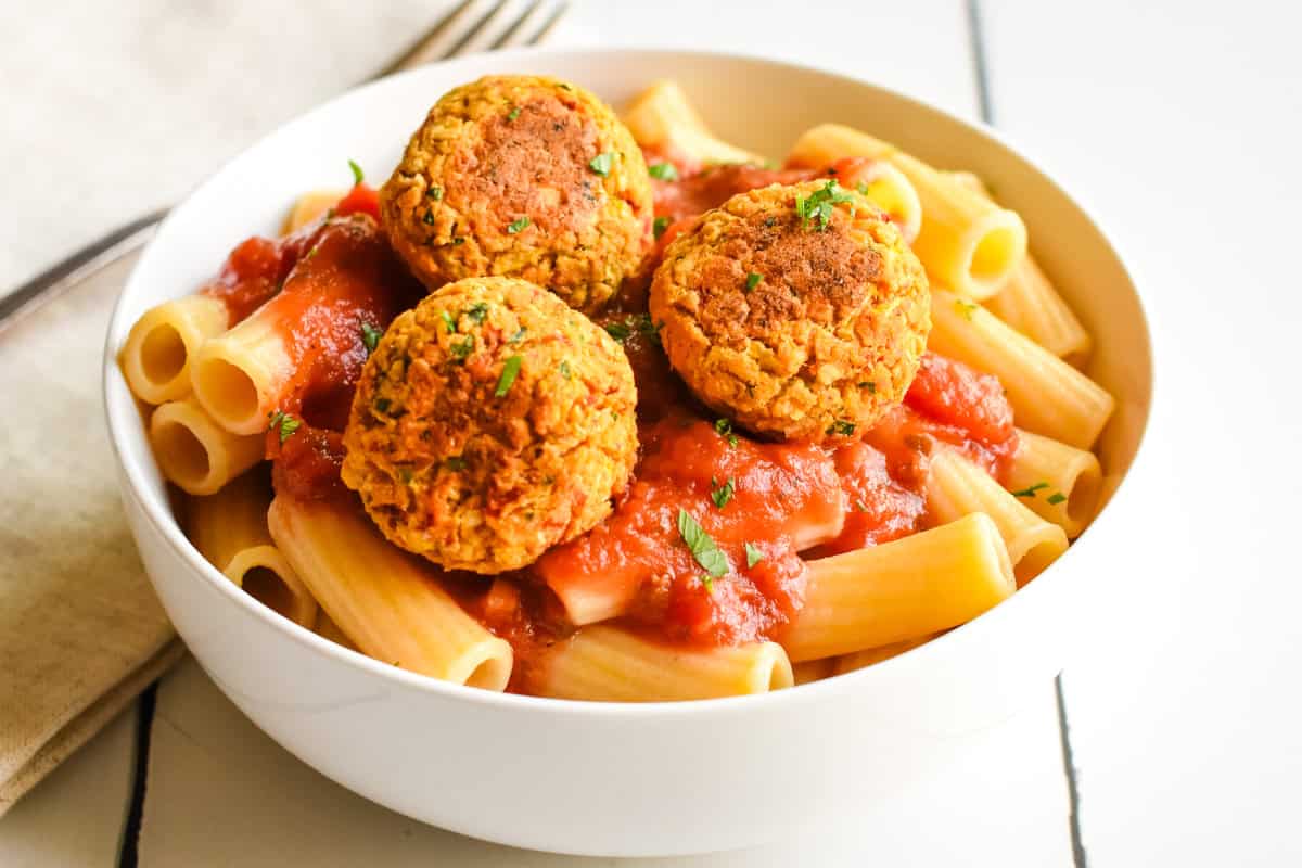 Chickpea balls sitting on top of rigatoni pasta and marinara sauce in a white bowl.