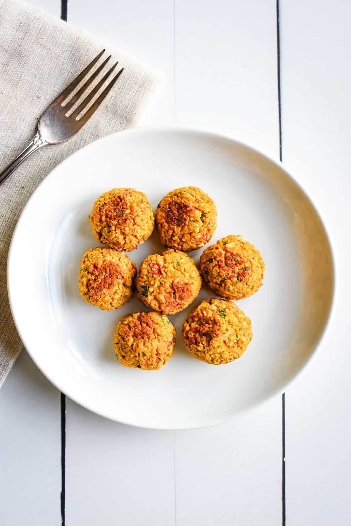 Three vegan meatballs made of chickpeas on top of pasta and sauce in a white bowl.