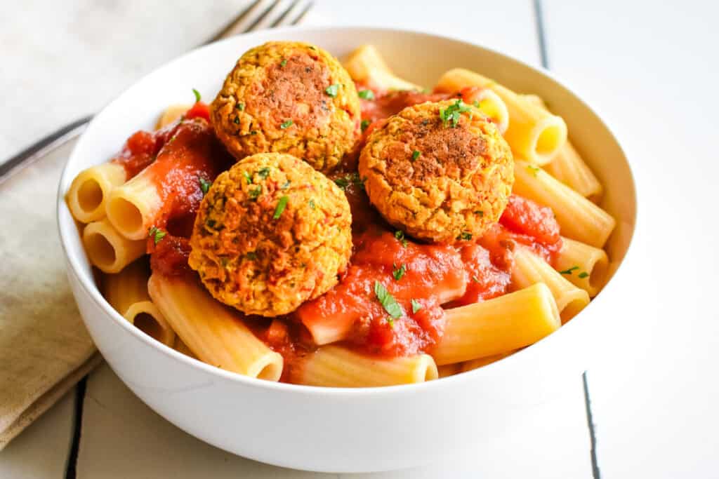Chickpea balls sitting on top of rigatoni pasta and marinara sauce in a white bowl.