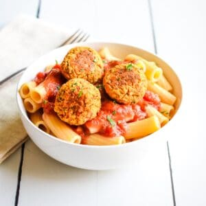 A white bowl of rigatoni pasta with marinara sauce topped with three chickpea balls.