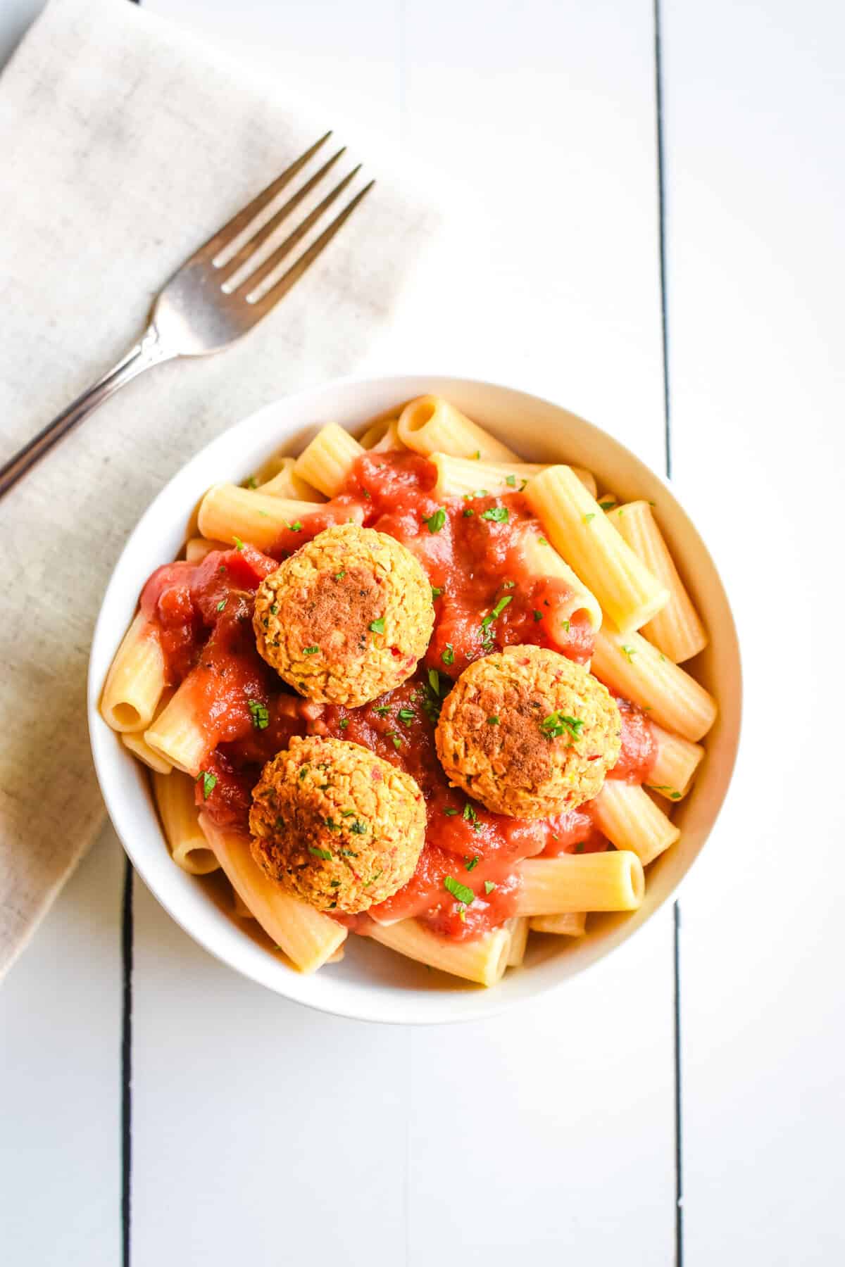 Three vegan meatballs made of chickpeas on top of pasta and sauce in a white bowl.