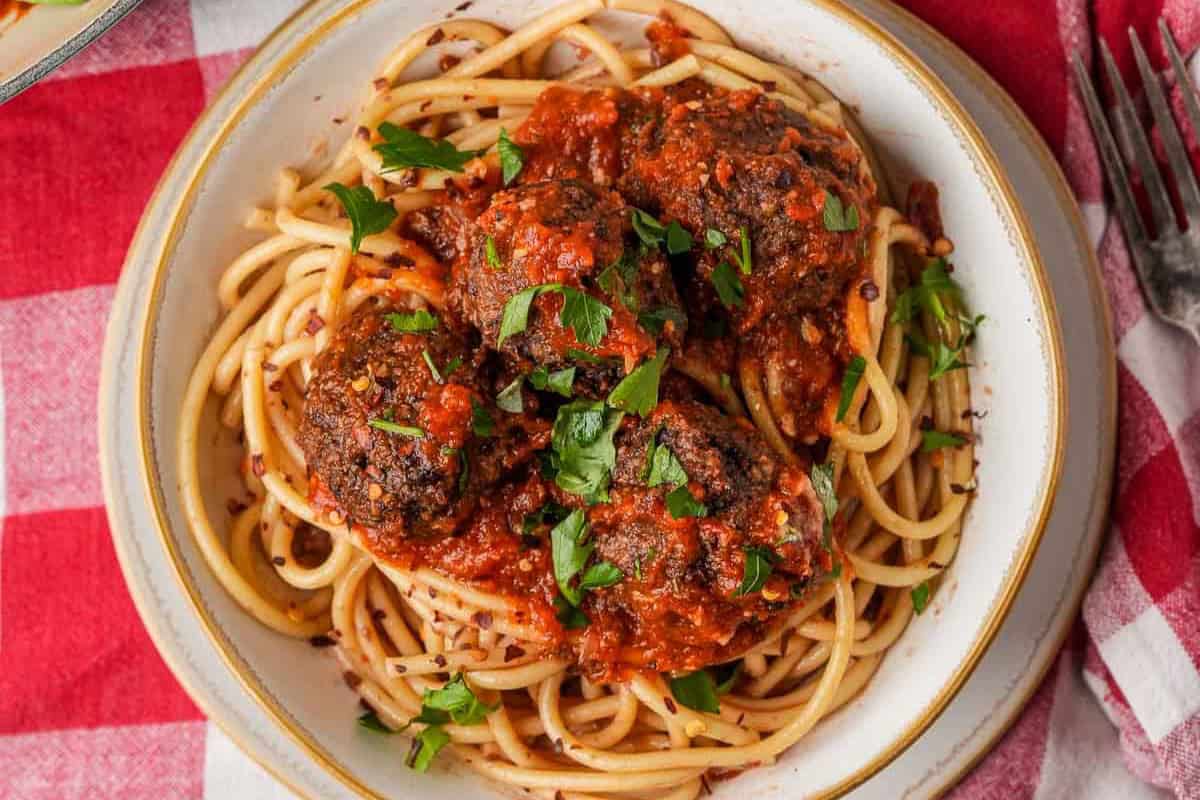 Spaghetti and vegan meatballs on a plate garnished with parsley.
