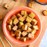 Tofu bites in an orange bowl on a wooden board.