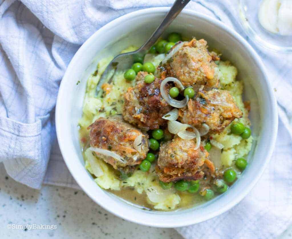 Vegan meatballs over mashed potatoes and gravy with peas in a bowl.