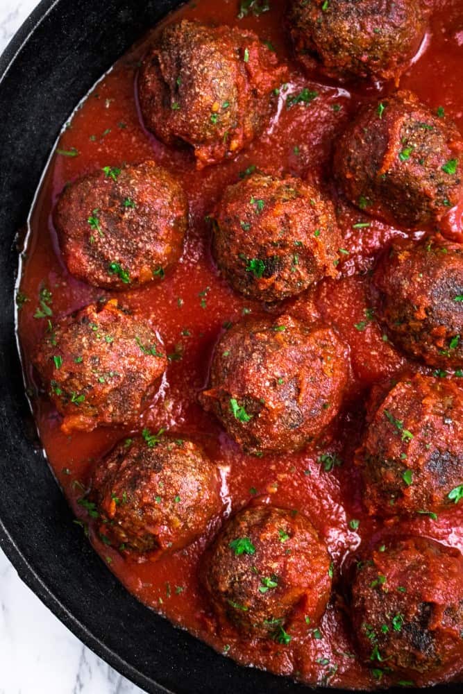 Close-up of TVP meatballs in a cast iron pan with marinara sauce.