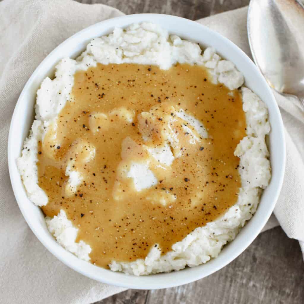 Gravy on top of mashed potatoes in a white bowl.