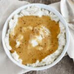 Gravy on top of mashed potatoes in a white bowl.