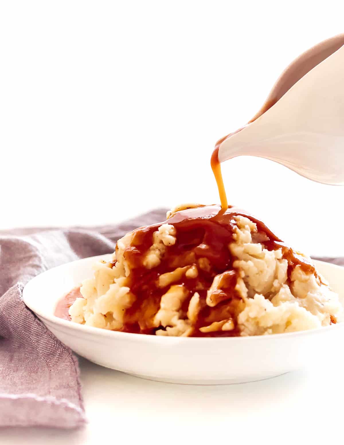 Pouring vegan red wine gravy onto a white dish of mashed potatoes.