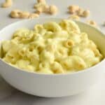 Close-up of cashew mac and cheese in a white bowl with cashews on the table behind it.