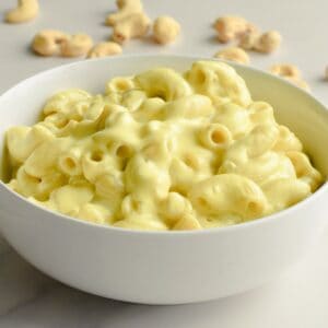 Close-up of cashew mac and cheese in a white bowl with cashews on the table behind it.