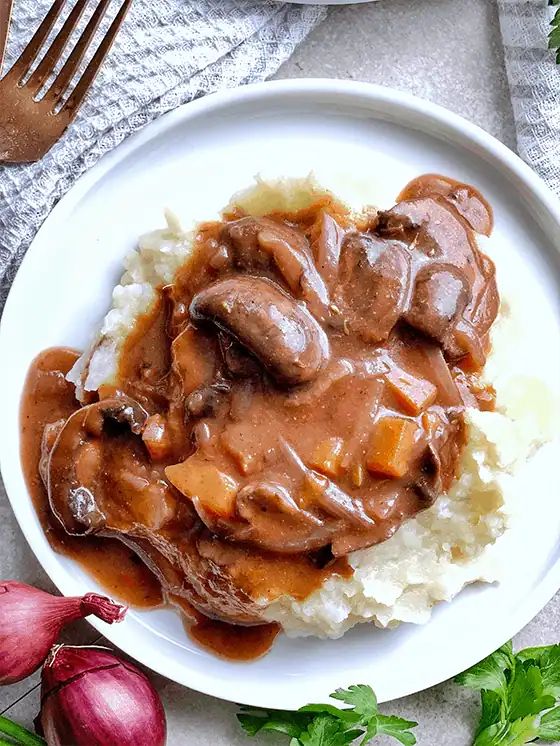 A serving of vegan mushroom burgundy on a bed of mashed potatoes on a white plate.