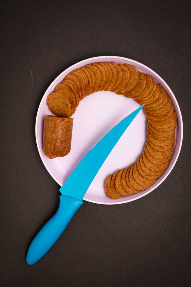 Sliced vegan pepperoni on a white plate with a blue knife.