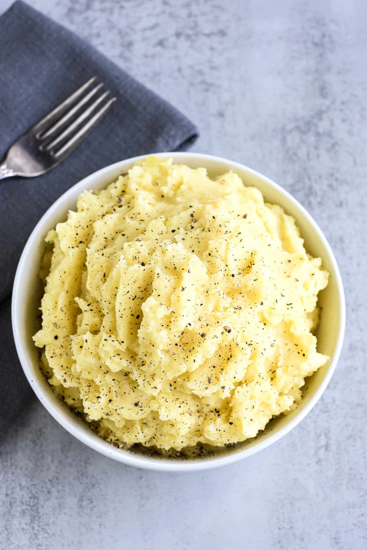 A white bowl filled with mashed potatoes garnished with black pepper.