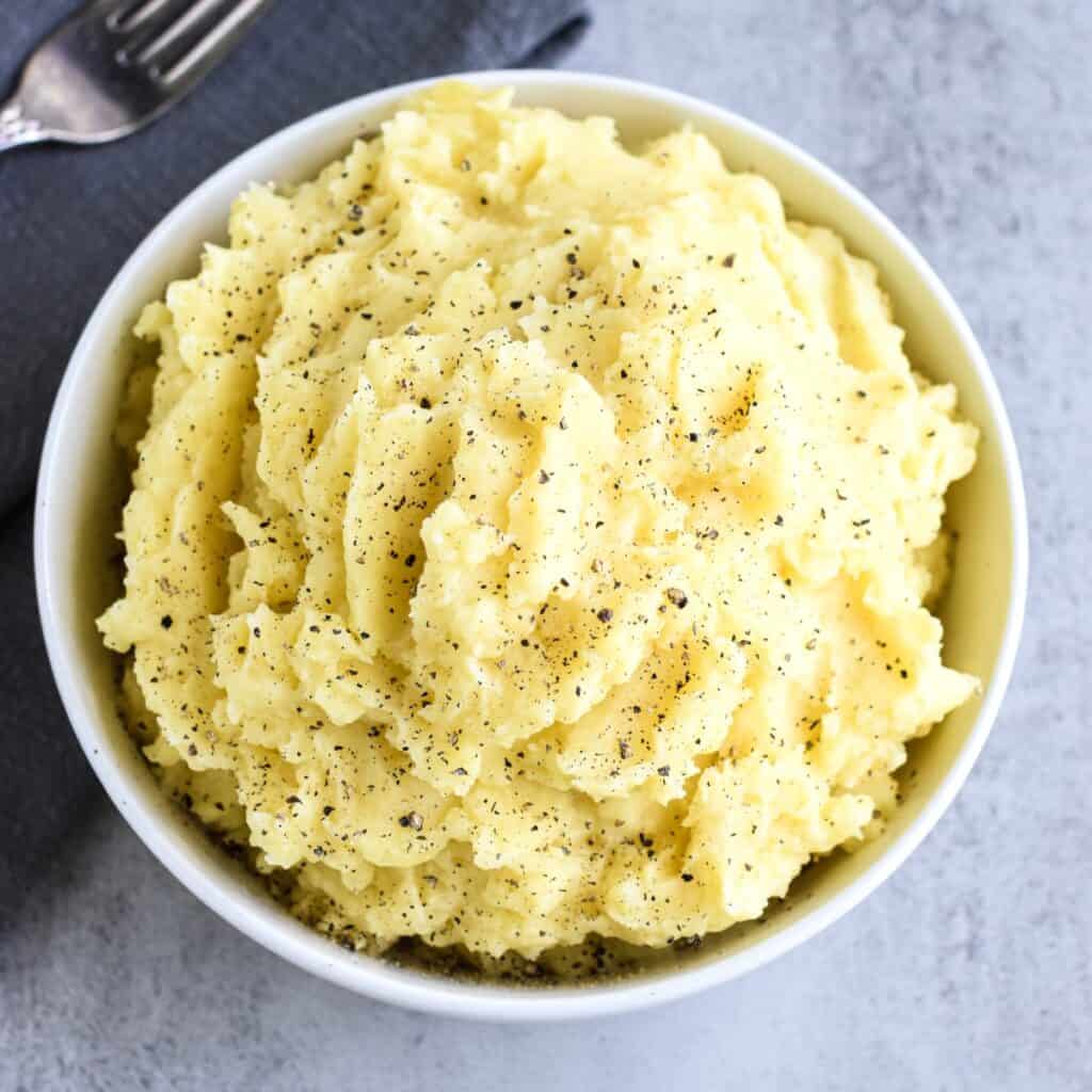 Close-up of mashed potatoes in a white bowl topped with black pepper.