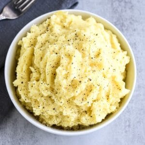 Close-up of mashed potatoes in a white bowl topped with black pepper.