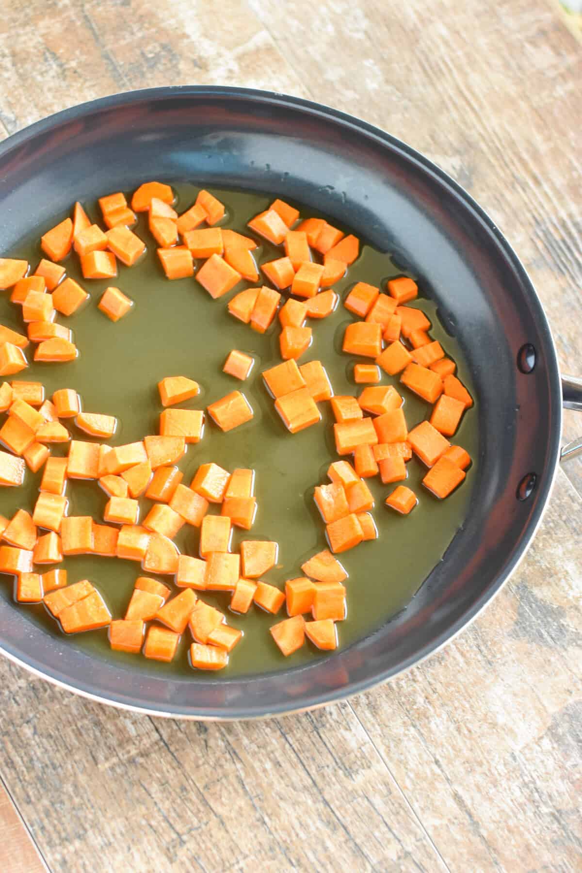 Diced carrots in vegetable broth in a nonstick skillet.