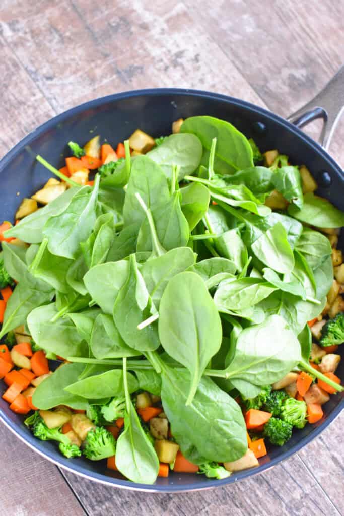 Baby spinach added to cooked veggies in a nonstick skillet.