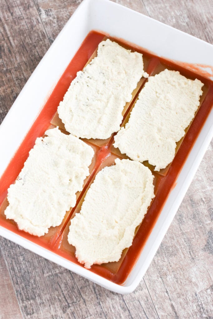 Almond ricotta spread onto lasagna sheets in a white casserole dish.