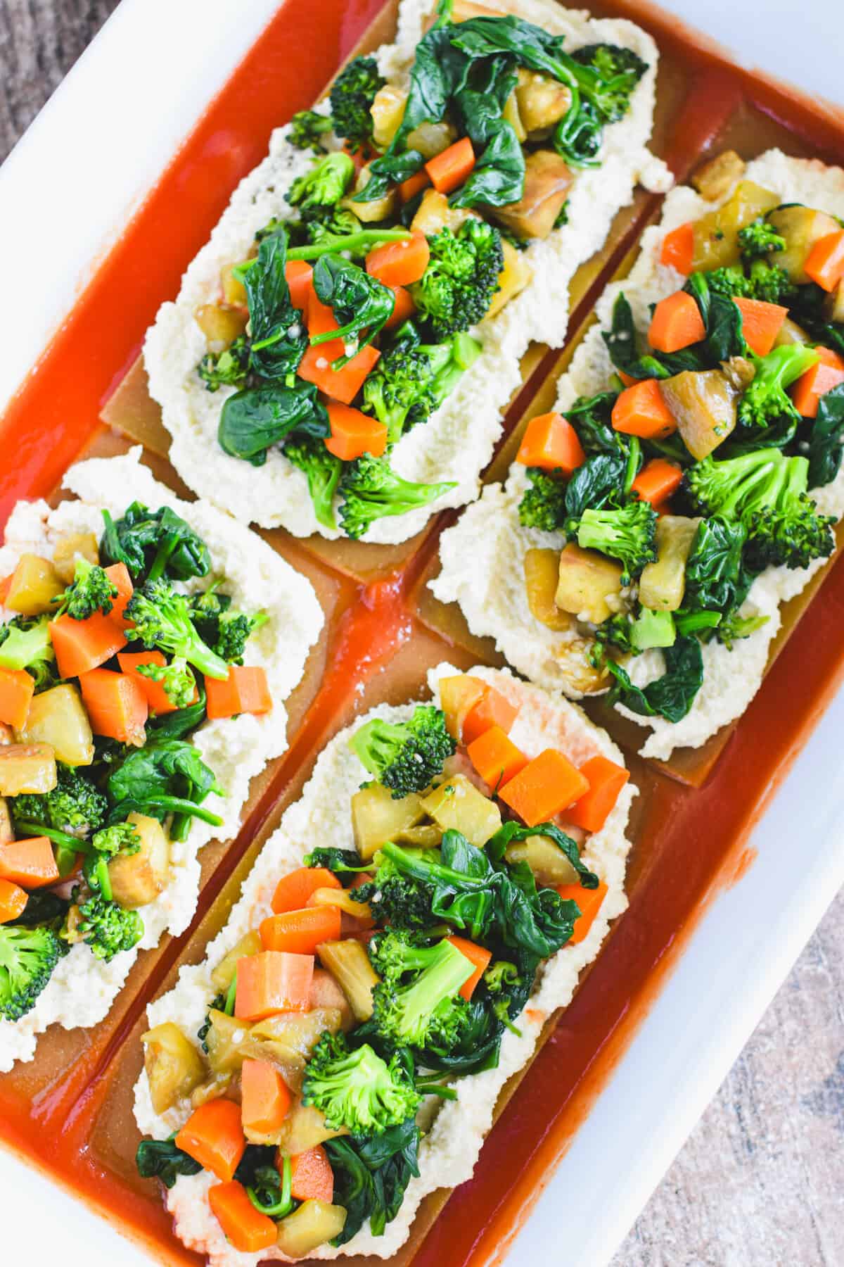 Sauteed veggies on top of vegan ricotta-lined lasagna sheets in a white casserole dish.