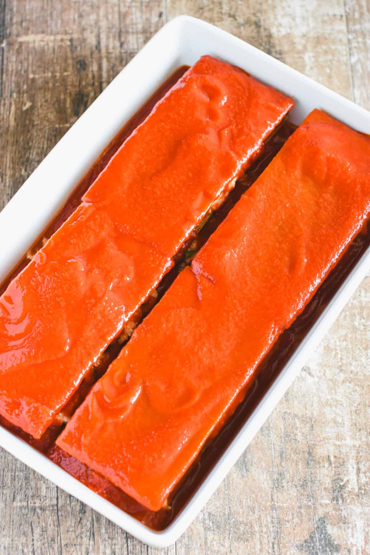 Tomato sauce covering two layers of lasagna in a white casserole dish.