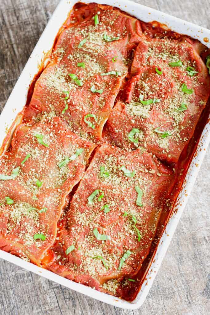 Lasagna garnished with vegan Parmesan-style cheese and basil in a white casserole dish.