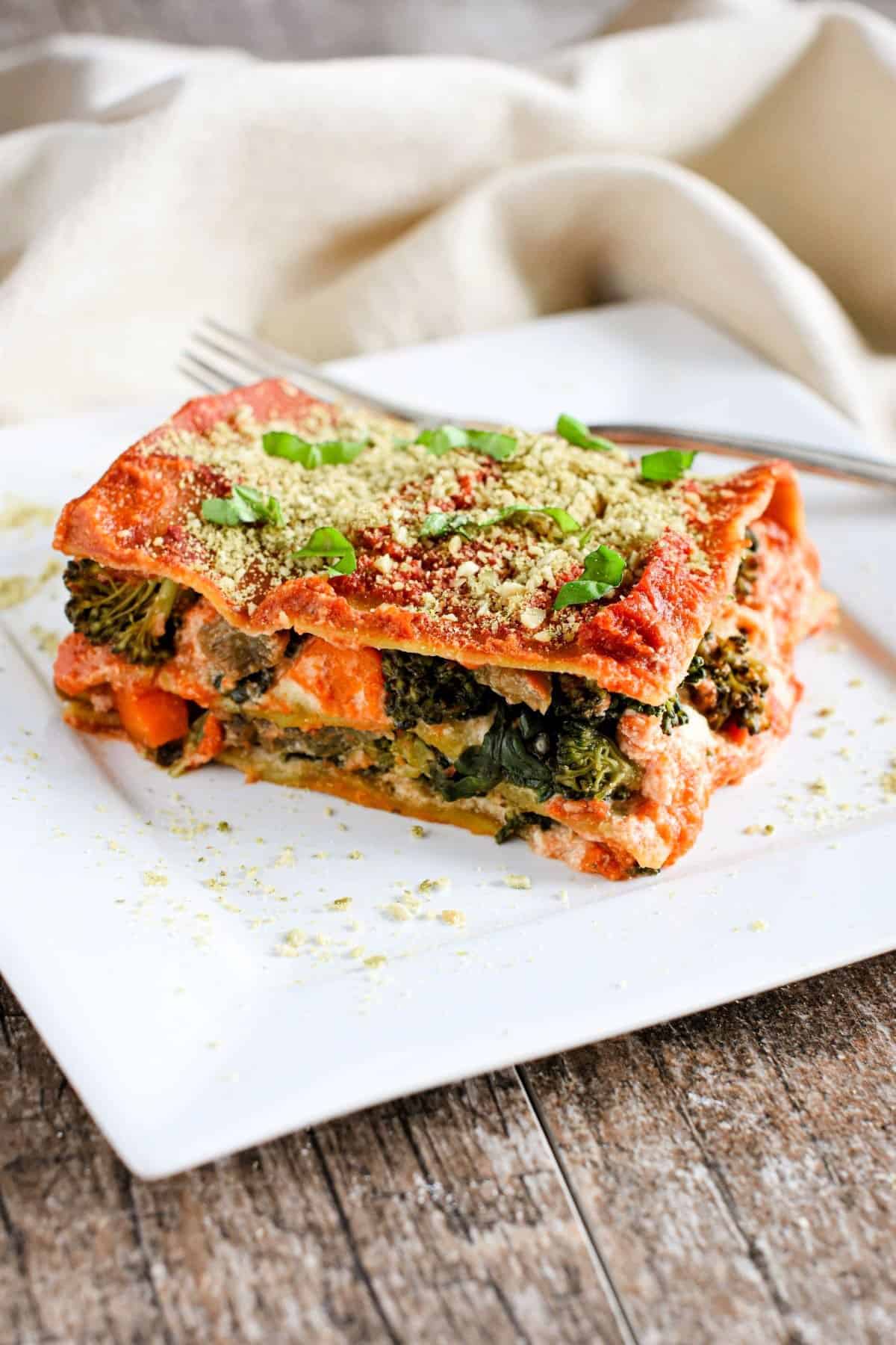 A square white plate with a slice of lasagna on it.
