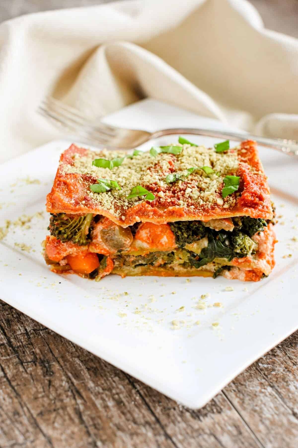 A slice of vegetable lasagna on a white plate with a fork behind it.