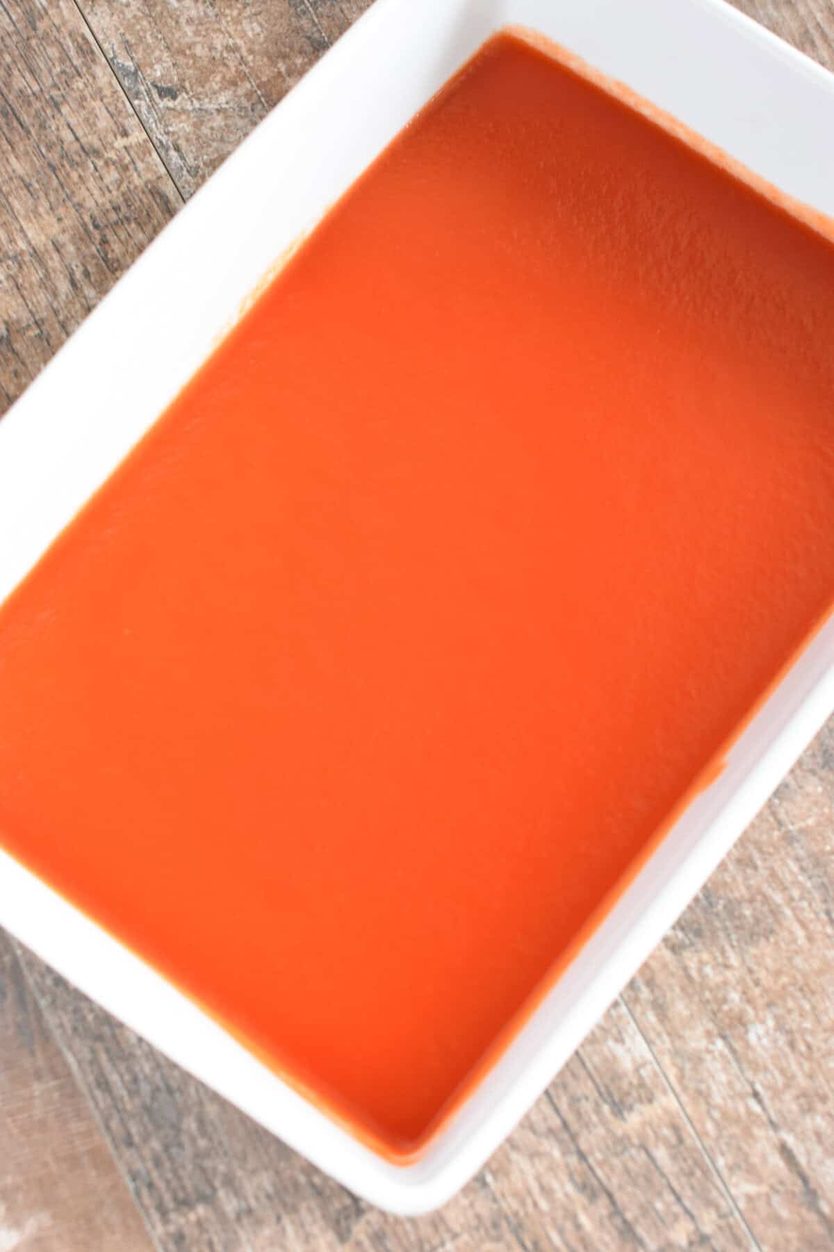 Tomato sauce in the bottom of a white casserole dish.