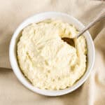 A white bowl with almond ricotta and a spoon in it sitting on a beige kitchen napkin.