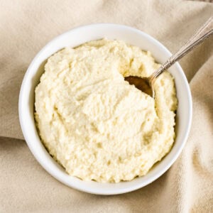 A white bowl with almond ricotta and a spoon in it sitting on a beige kitchen napkin.
