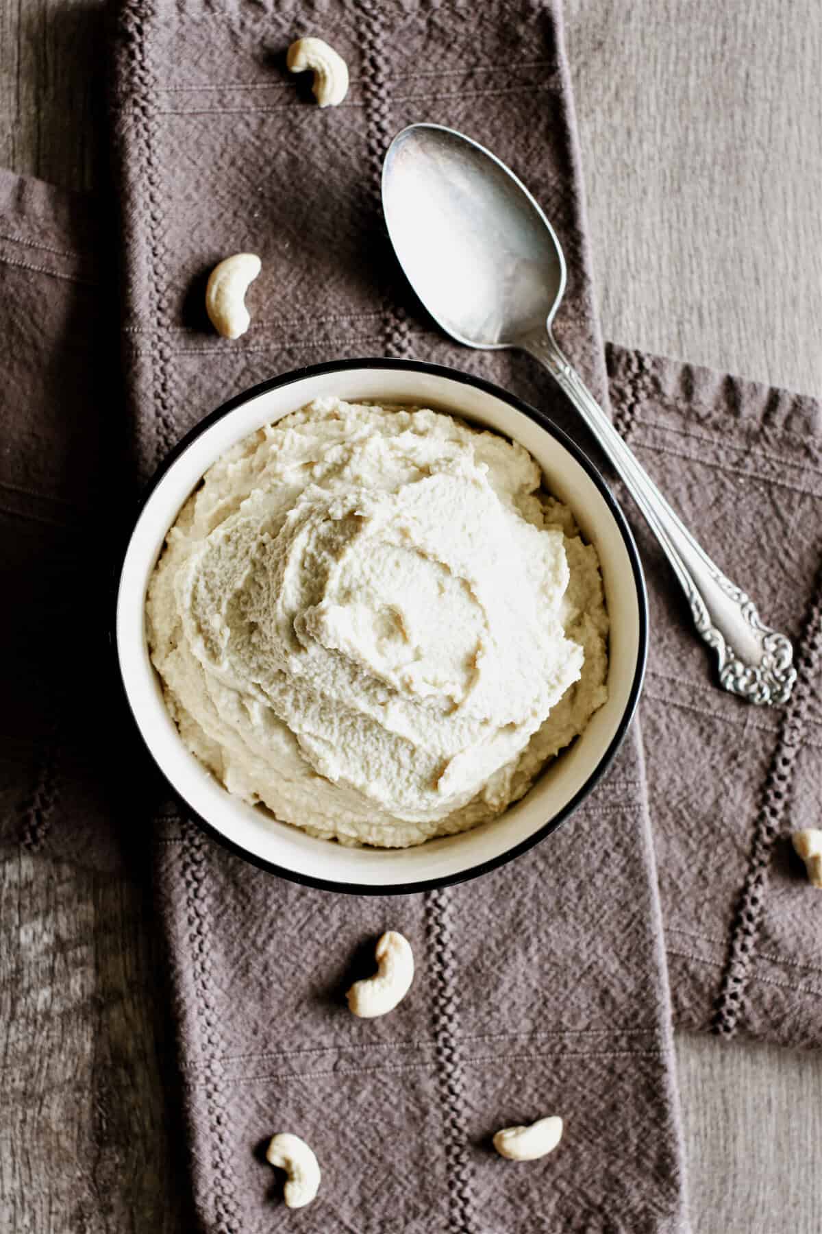 Non-dairy ricotta in a bowl on a kitchen napkin with cashews on it and a spoon.