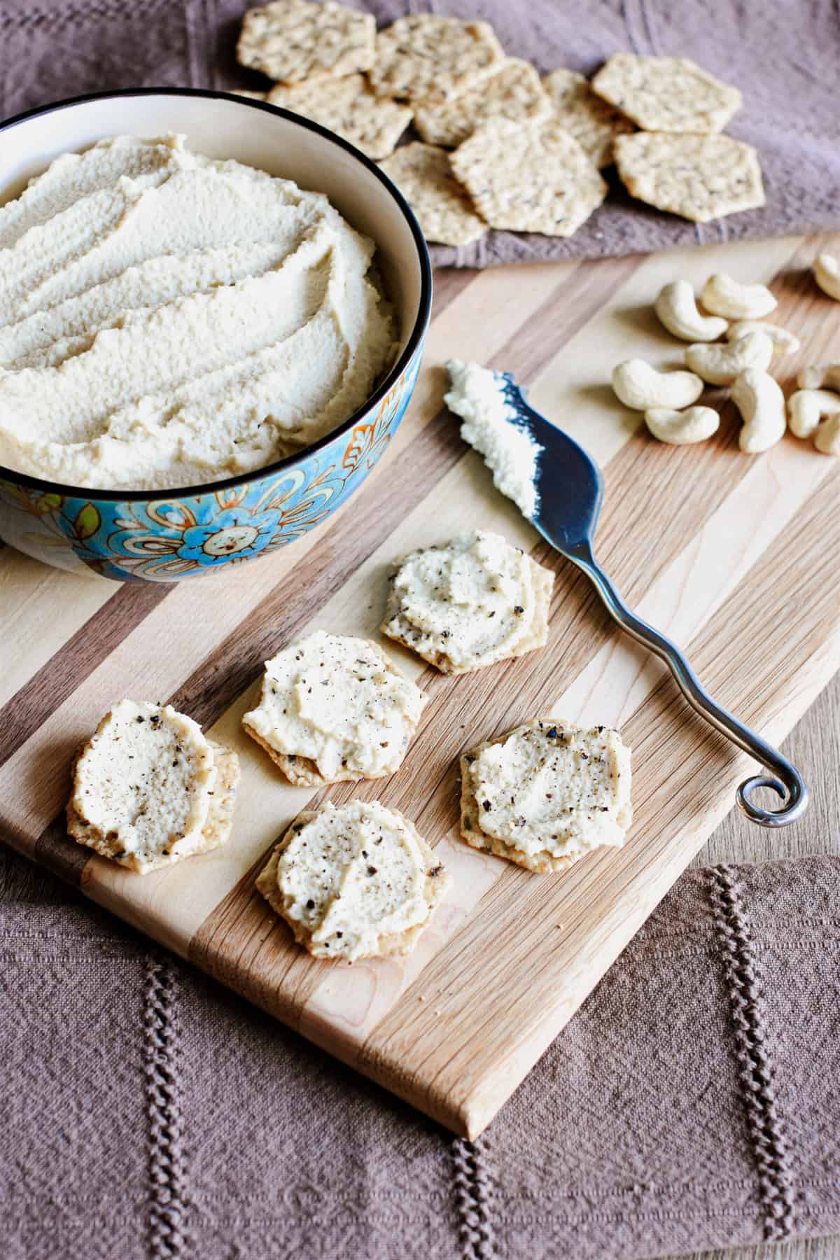 Cashew ricotta cheese in a bowl and some on crackers on a wooden board.