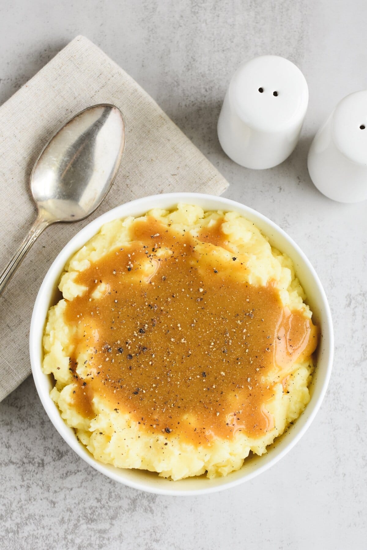 A bowl of mashed potatoes topped with gravy and black pepper.