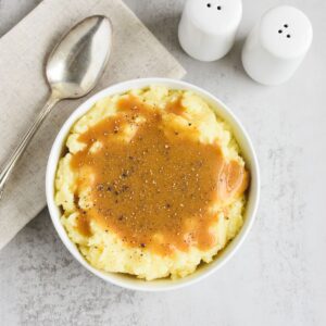 Gravy and black pepper on top of a bowl of mashed potatoes.