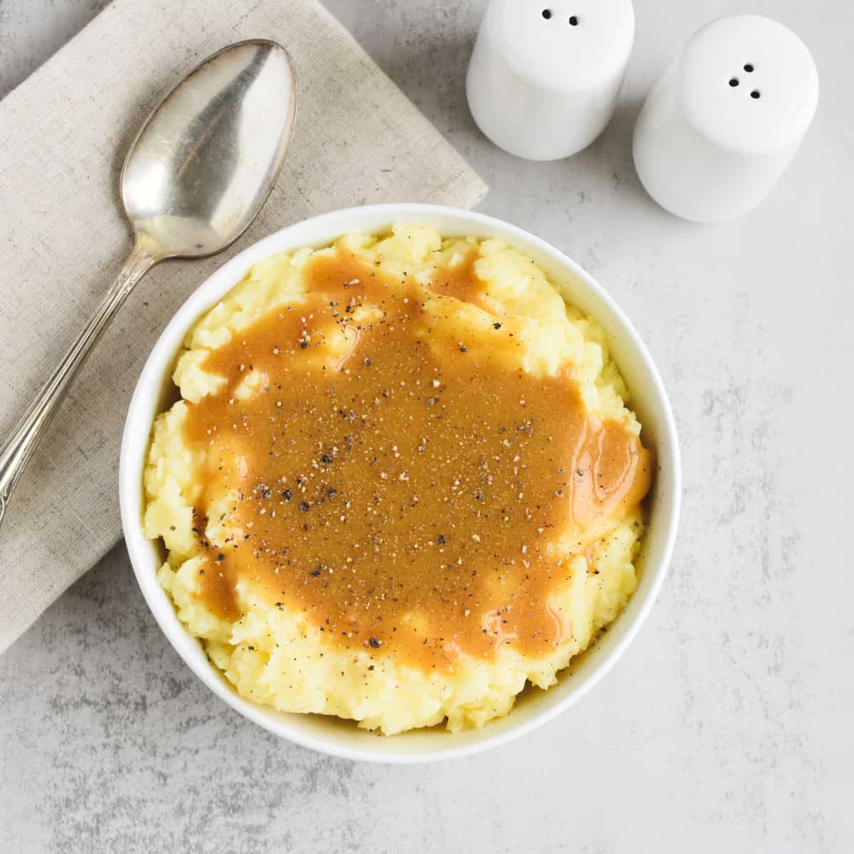 Gravy and black pepper on top of a bowl of mashed potatoes.